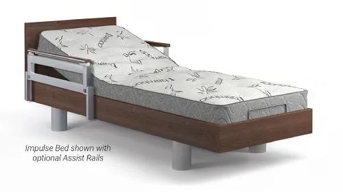 A wooden-frame adjustable bed with a patterned mattress and metal assist rails on the side. Text reads: "Impulse Bed shown with optional Assist Rails.