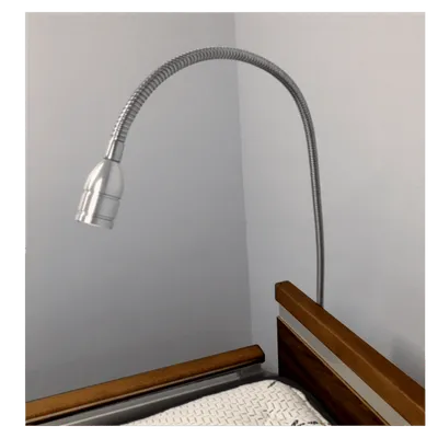 A flexible desk lamp, #15395, overhanging a wooden bedside table against a grey wall.