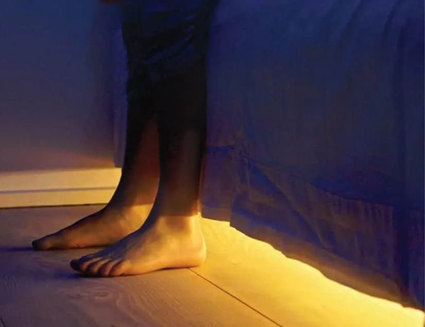 SonderCare motion-activated underbed nightlight glowing beneath a bed frame