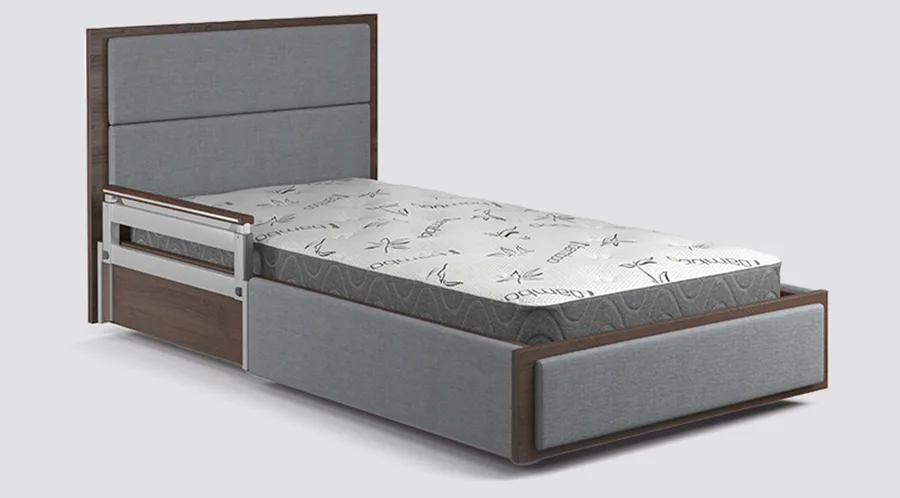 Single bed with a padded headboard and footboard, side safety rail, and a mattress featuring a patterned cover, all in gray and brown tones.