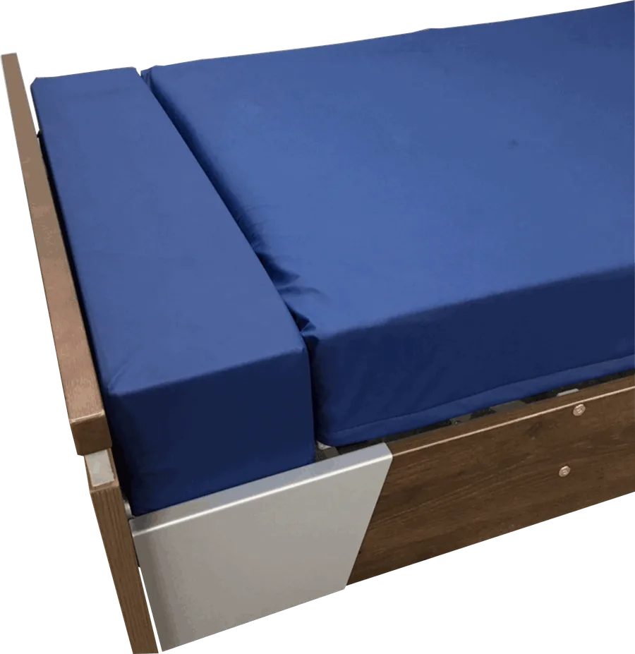 A wooden bed frame with a blue mattress and with mattress extension at the end of the bed. 