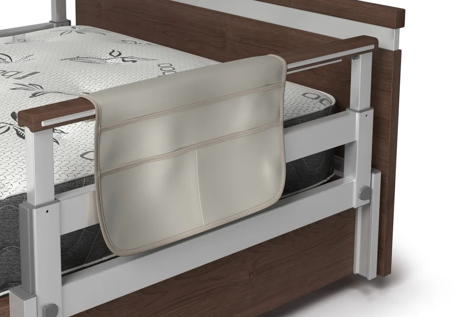 A beige organizer pouch hanging on the wooden side rail of a bed with a patterned mattress.