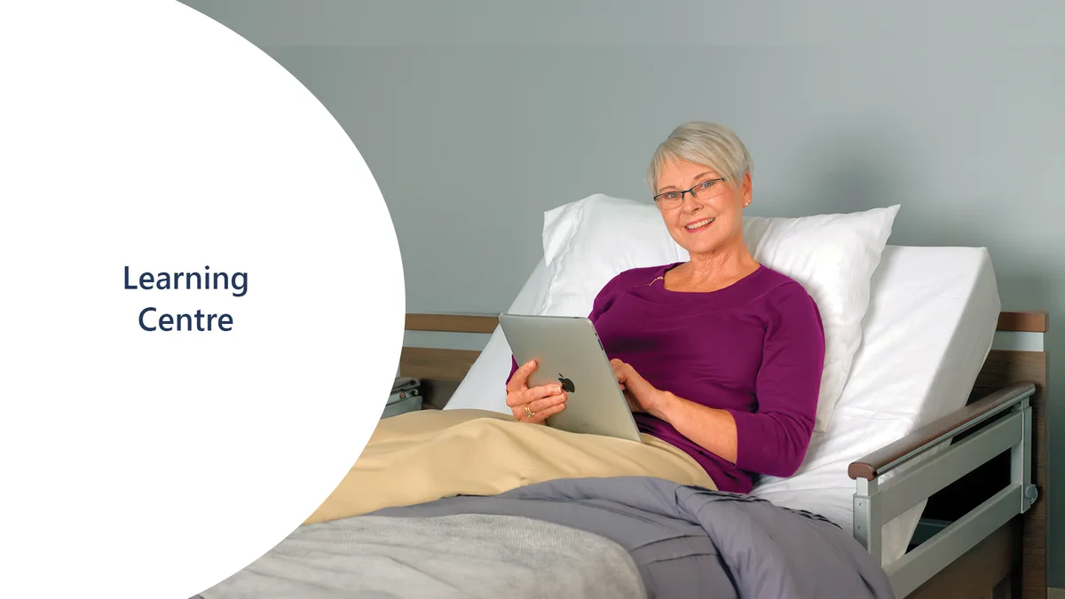An older woman with short gray hair sits up in a hospital bed, smiling and using a tablet. The text "Learning Centre" appears on a white background next to her.